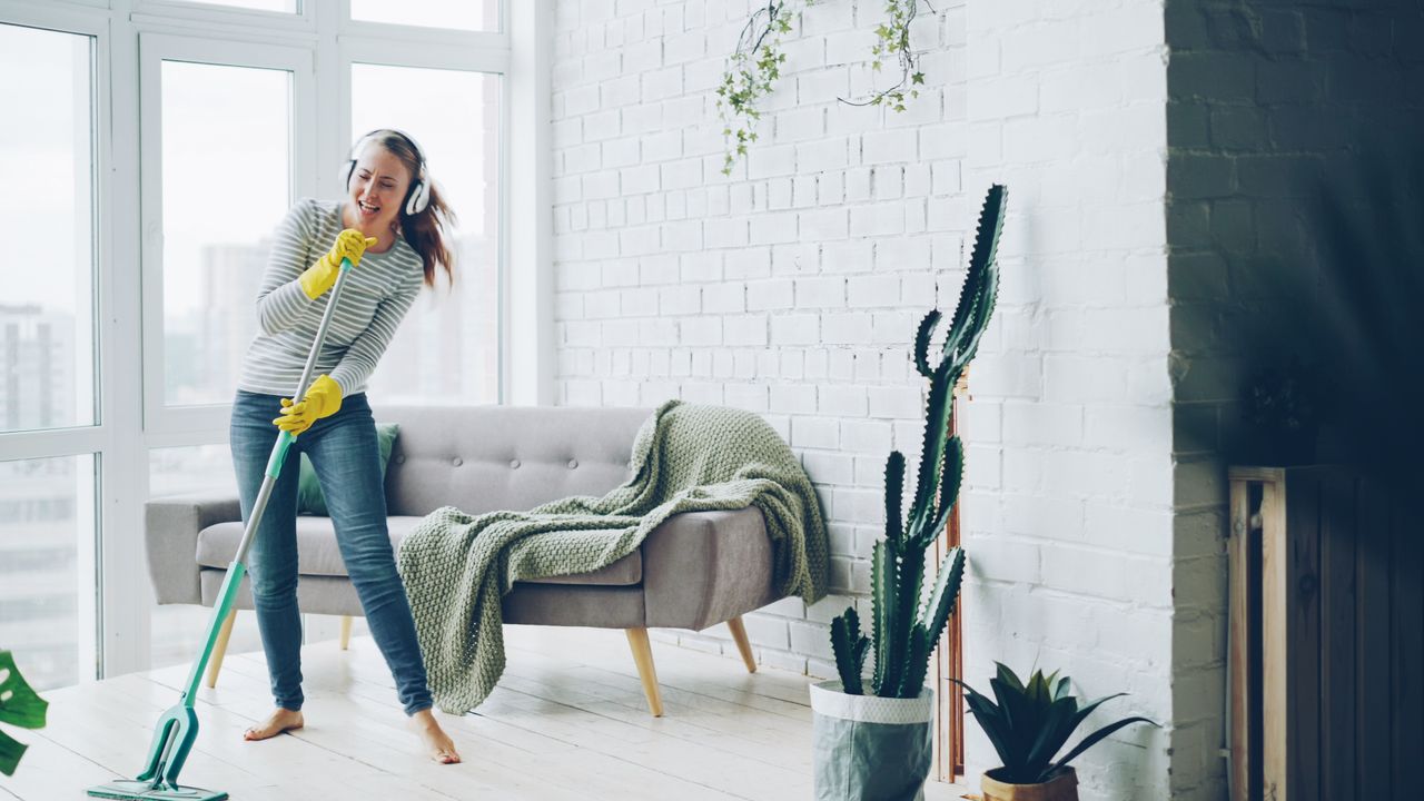 Happy woman listening to music while mopping a modern living room.