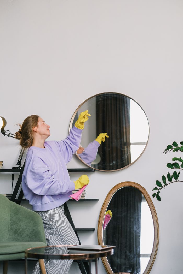 Side view of cheerful young female in casual clothes and yellow latex gloves standing near mirrors and dancing while cleaning apartment in daytime